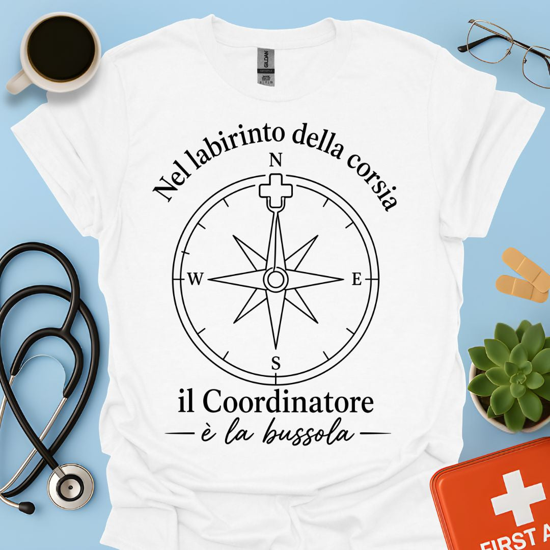 Maglietta t-shirt bianca a maniche corte da infermiere con grafica nera di una bussola e la frase: "Nel labirinto della corsia il Coordinatore è la bussola" con ago a forma di croce medica.